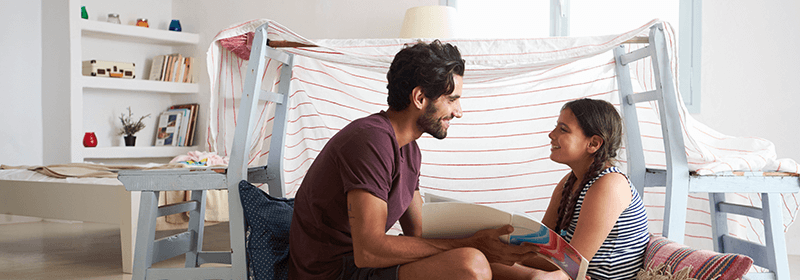 Father reading book to daughter in blanket fort