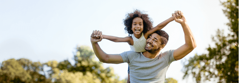 Dad holding daughter on shoulders outside