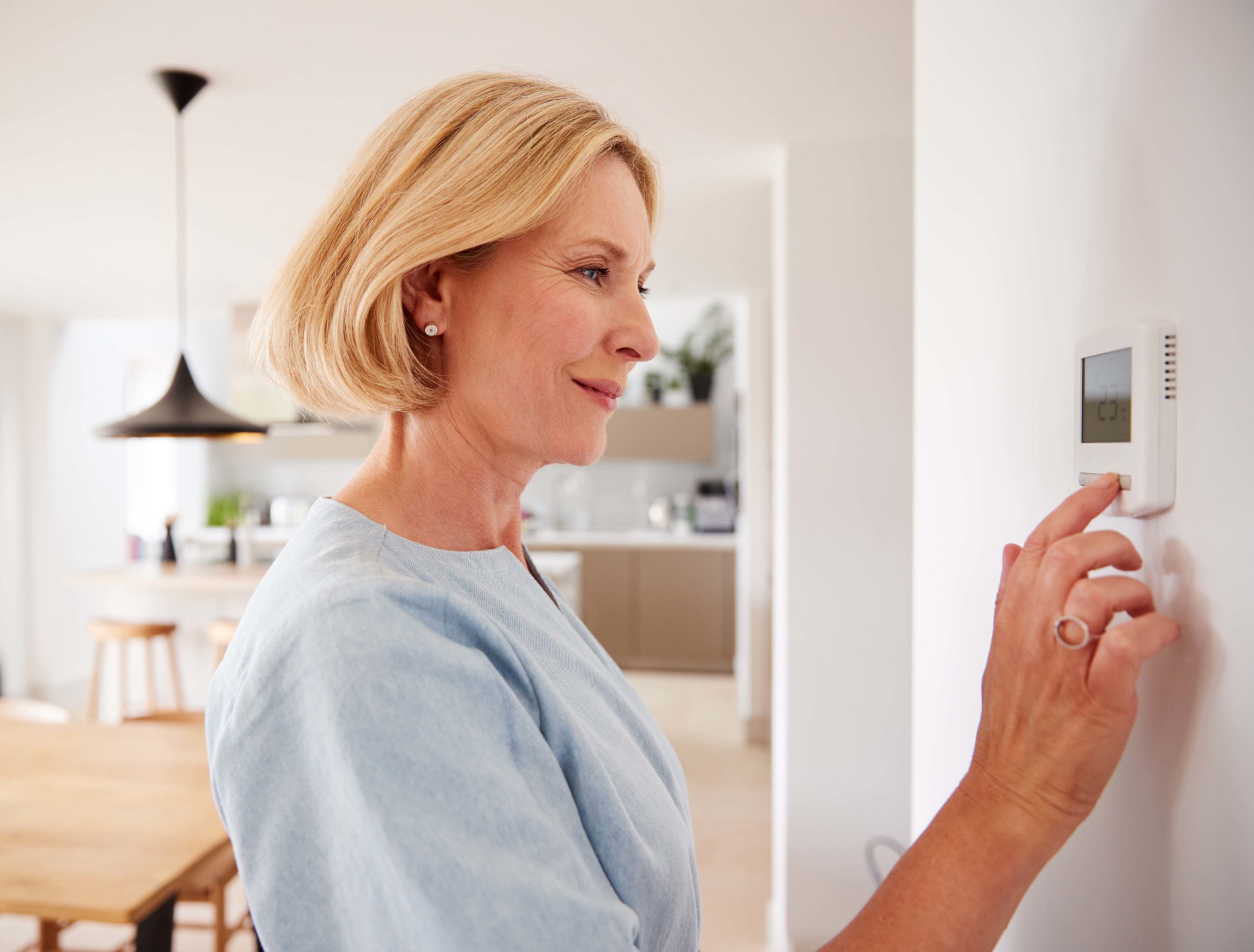 Smiling woman adjusting thermostat in her home