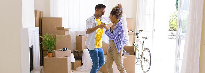 A couple dancing in their living room, surrounded by moving boxes.