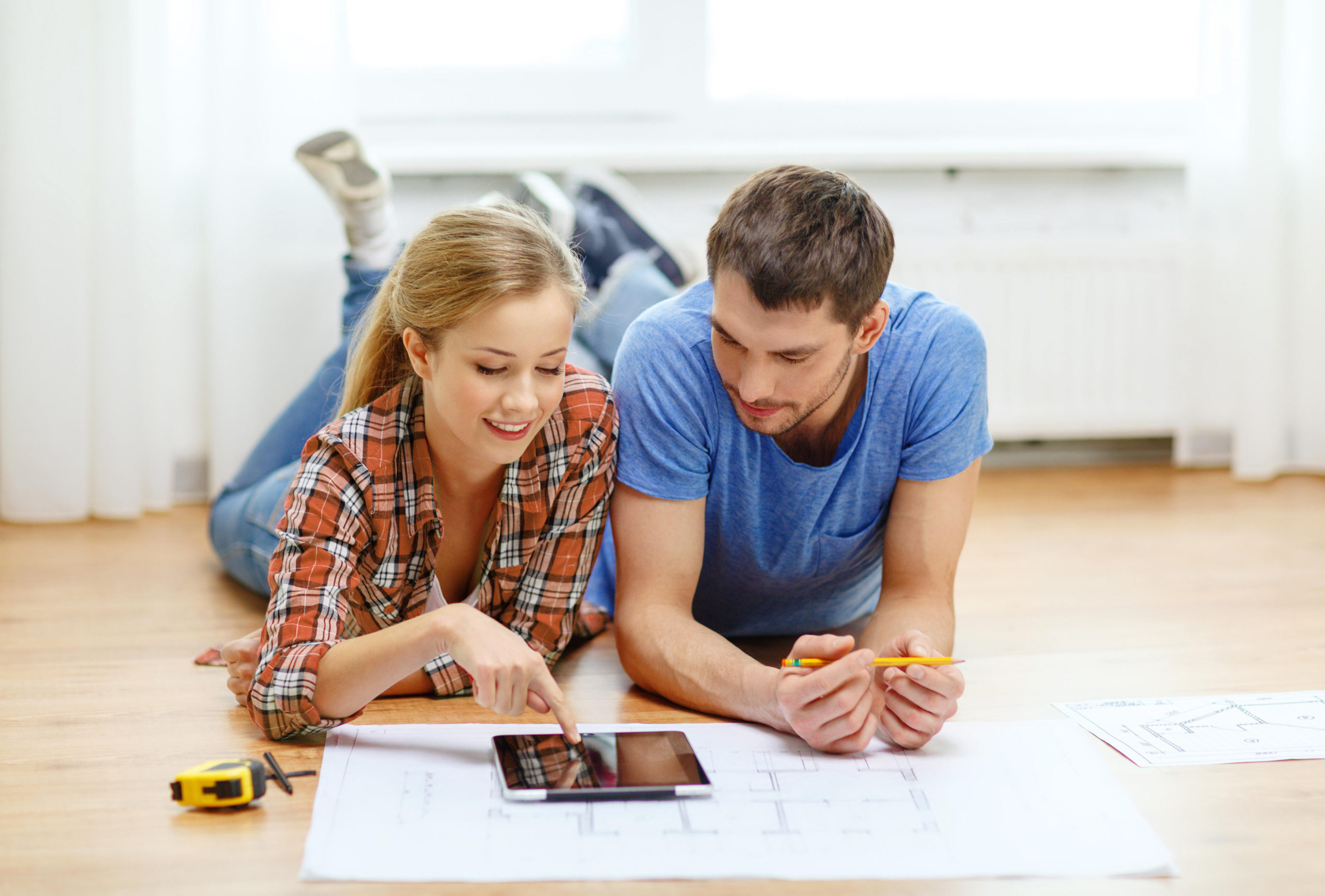 Smiling couple laying on floor looking at blueprints