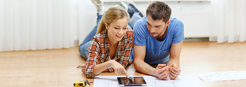 Couple laying on floor of home looking at blueprints